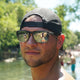 Man wearing black mens trucker hats with adjustable snapback and sunglasses outdoors near water and trees