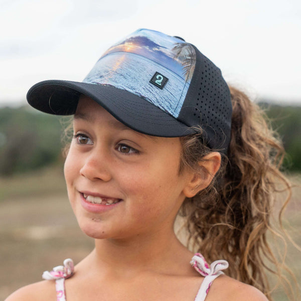 Youth girls wearing Seas the Day Girl Trucker Hat with high ponytail opening and coastal design