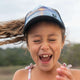 Girls Trucker Hat wearing Seas the Day high ponytail trucker cap with scenic print, smiling outdoors