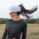 Woman wearing white Aoraki Ponytail Womens Trucker Hat with high ponytail opening outdoors in nature