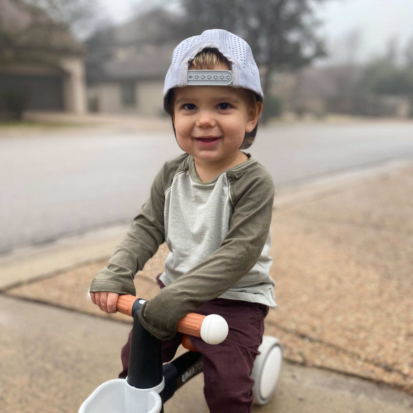 Toddler wearing a white Boys trucker cap backwards while riding a toy bike outdoors, suitable for performance mountain trucker hat use