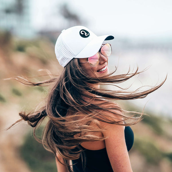 White Aoraki Ponytail Womens Trucker Hat with breathable mesh and high ponytail opening, worn outdoors by woman with flowing hair