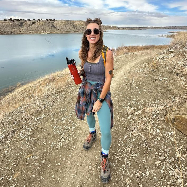 girl outside next to a lake holding a stainless steel water bottle with storage from Puddles 2 Oceans