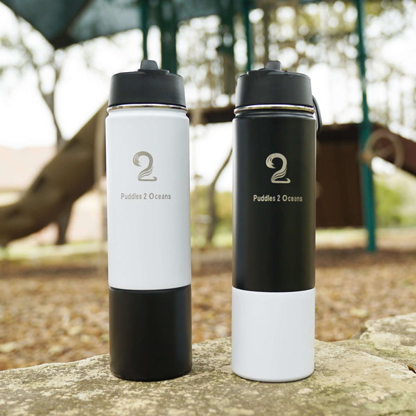 Two double-walled insulated kids water bottles with storage compartments and customizable colored bottoms standing outdoors