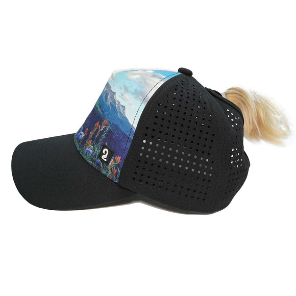 Female trucker hat with high ponytail opening, breathable black mesh, and scenic mountain print panel