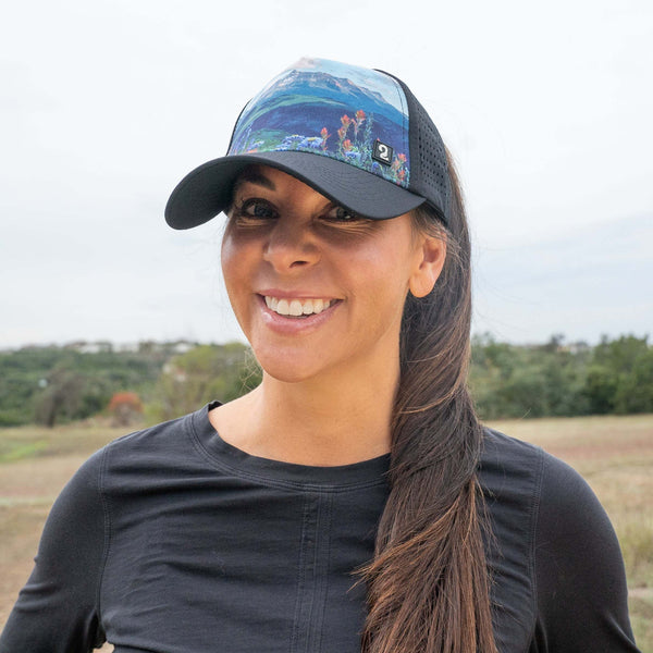 Smiling woman wearing a "Flowers in Her Hair" female trucker hat with a high ponytail opening outdoors